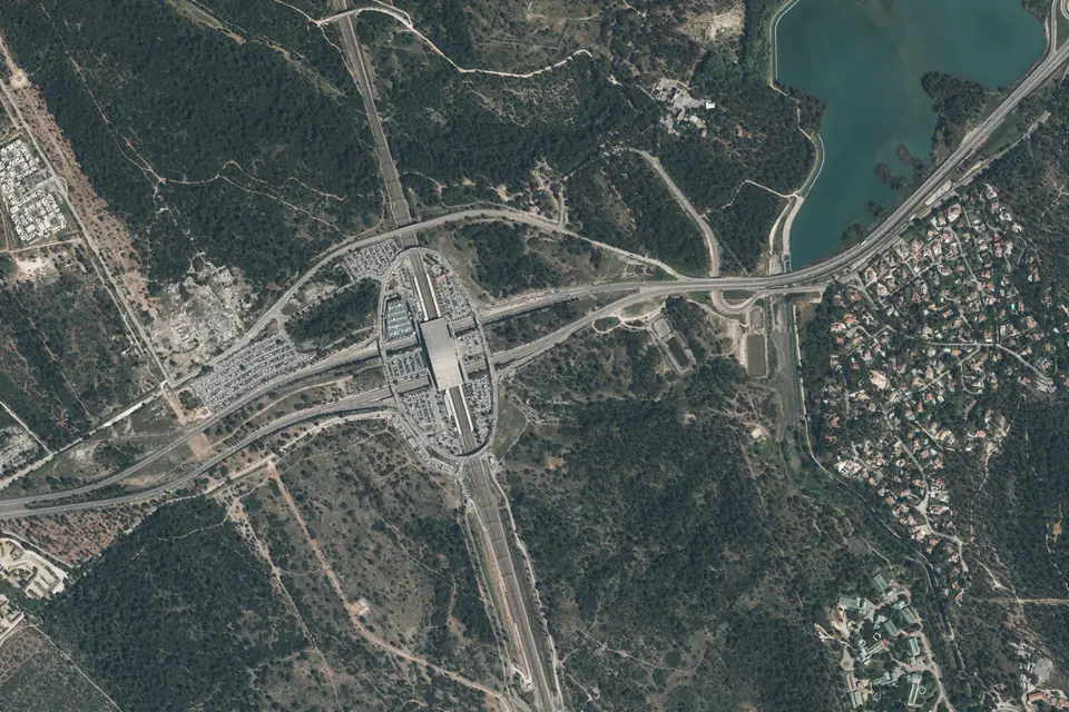 Vue aérienne de la gare d’Aix-en-Provence TGV au milieu de la garrigue, entourée de parkings et de routes, avec des maisons à droite