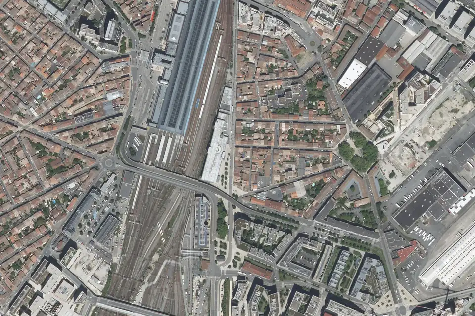 Vue aérienne de la gare Bordeaux Saint-Jean : la halle et les voies au centre, le pont du Guit qui les croise, et les maisons basses du quartier Belcier à droite